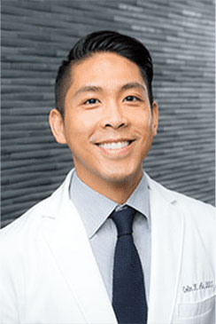 A man in a white lab coat is smiling and looking directly at the camera.