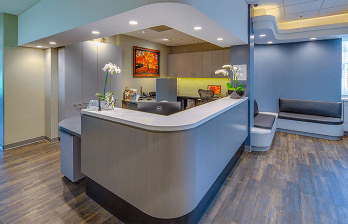 An image of a modern reception area with a curved counter and a waiting bench, featuring a colorful wall decoration.