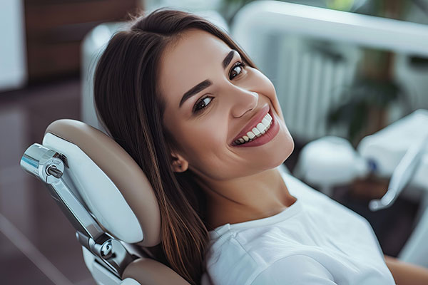 A woman sitting in a dental chair with a smile on her face, looking directly at the camera.
