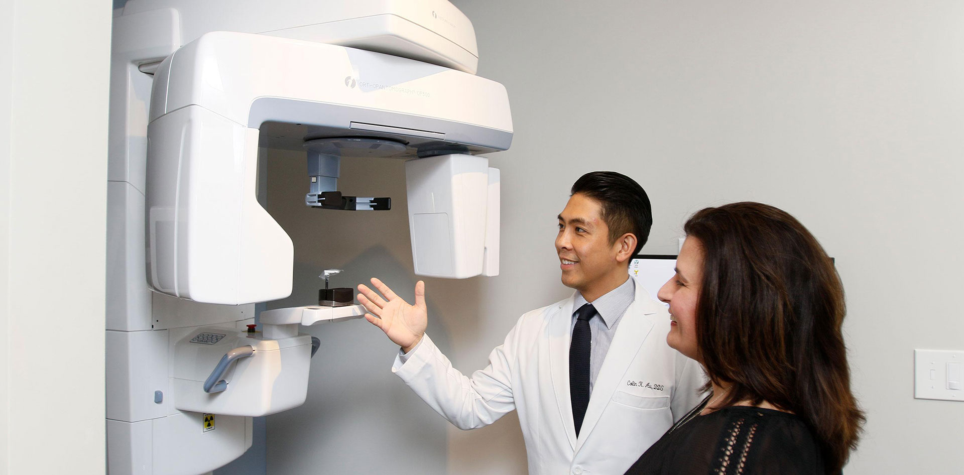 Medical professional in front of a large, modern dental X-ray machine, with two individuals observing the equipment.