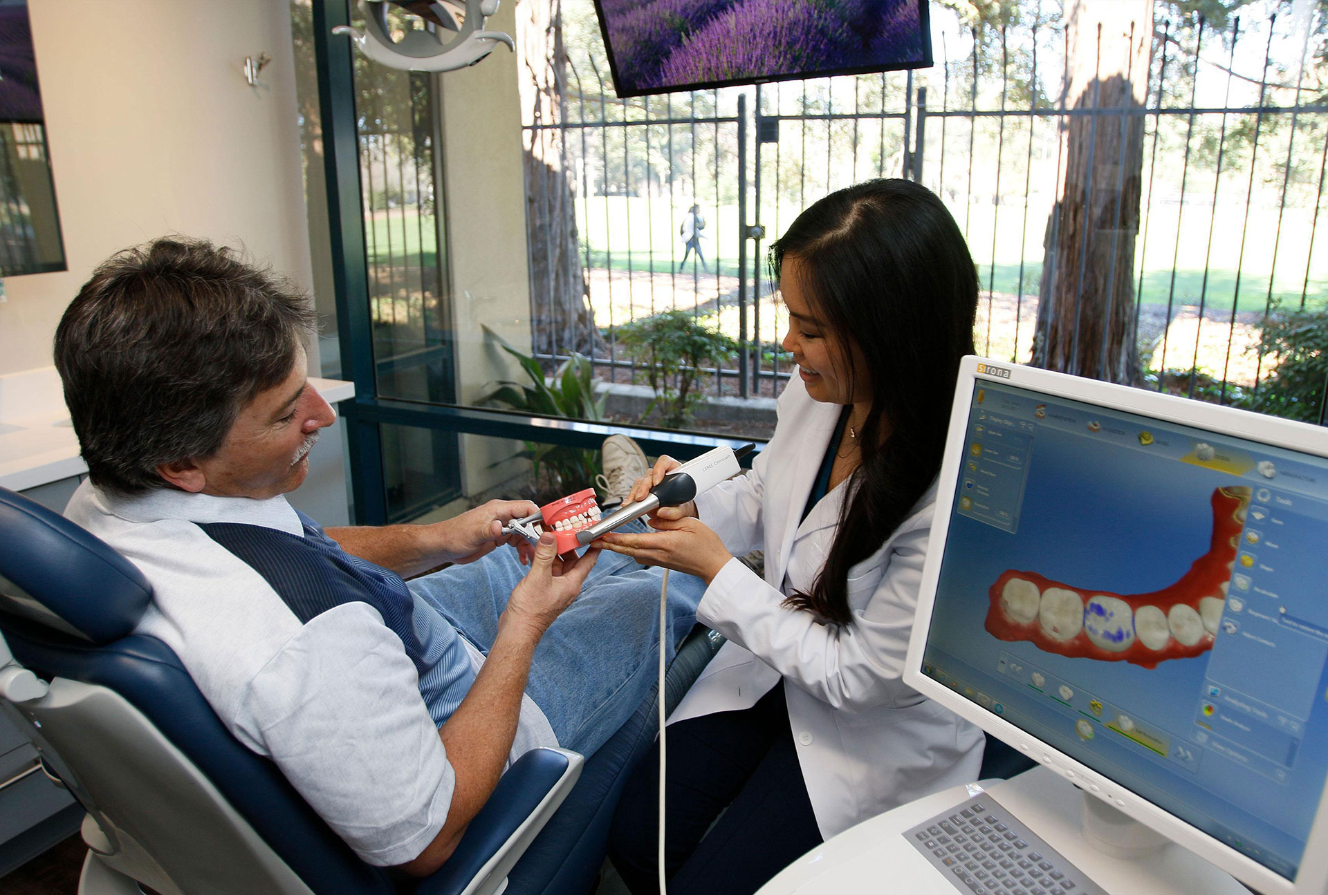 The image shows a dental patient receiving treatment from a dentist, with a monitor displaying the patient s mouth and teeth.