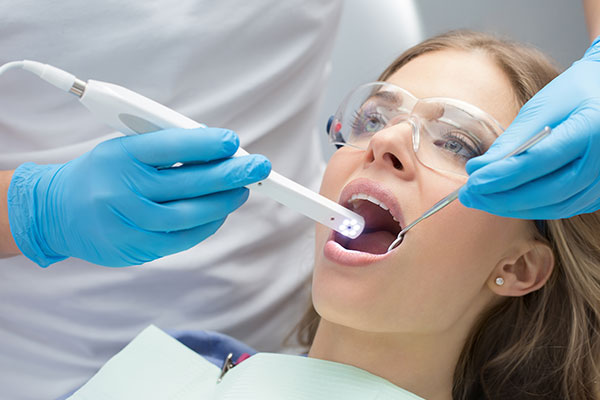 A dental hygienist is performing a teeth cleaning procedure on a patient in a dental office, using an electronic device to clean the teeth.