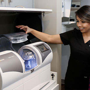 A woman in a white lab coat stands beside an open dental equipment cabinet, inspecting the contents.