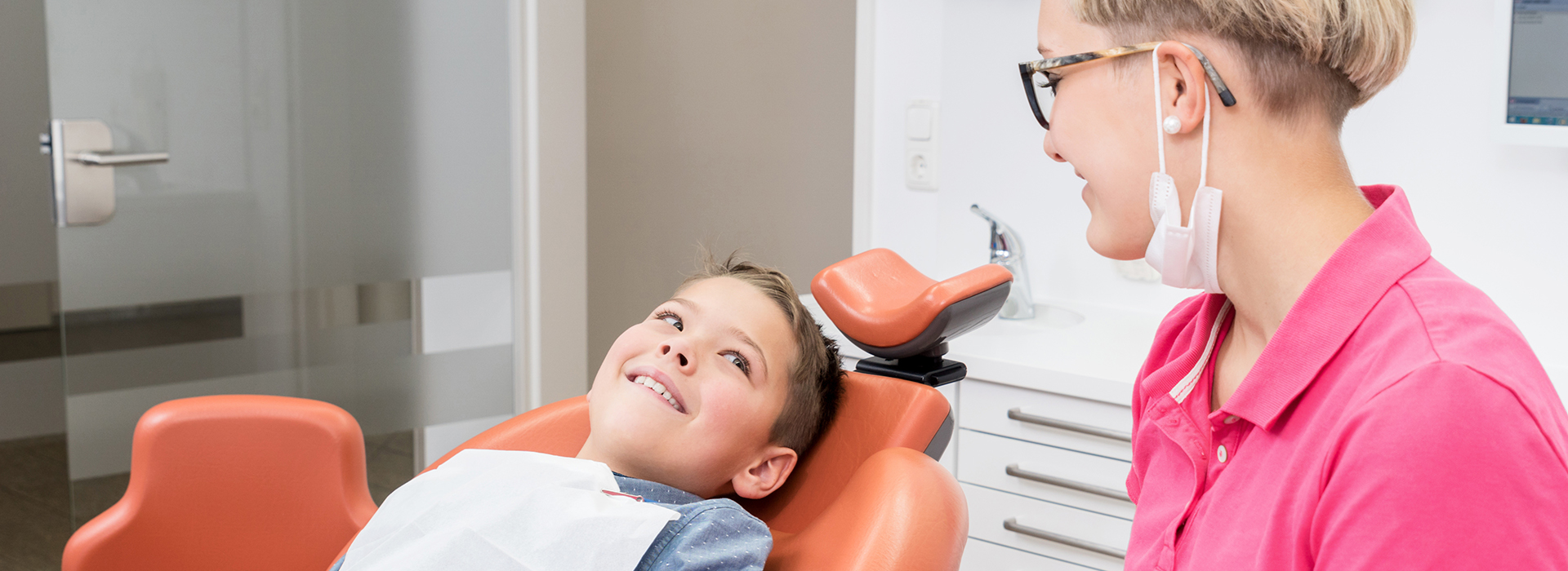 A dental office scene, featuring a dentist and a child in a chair, with the child smiling at the camera.
