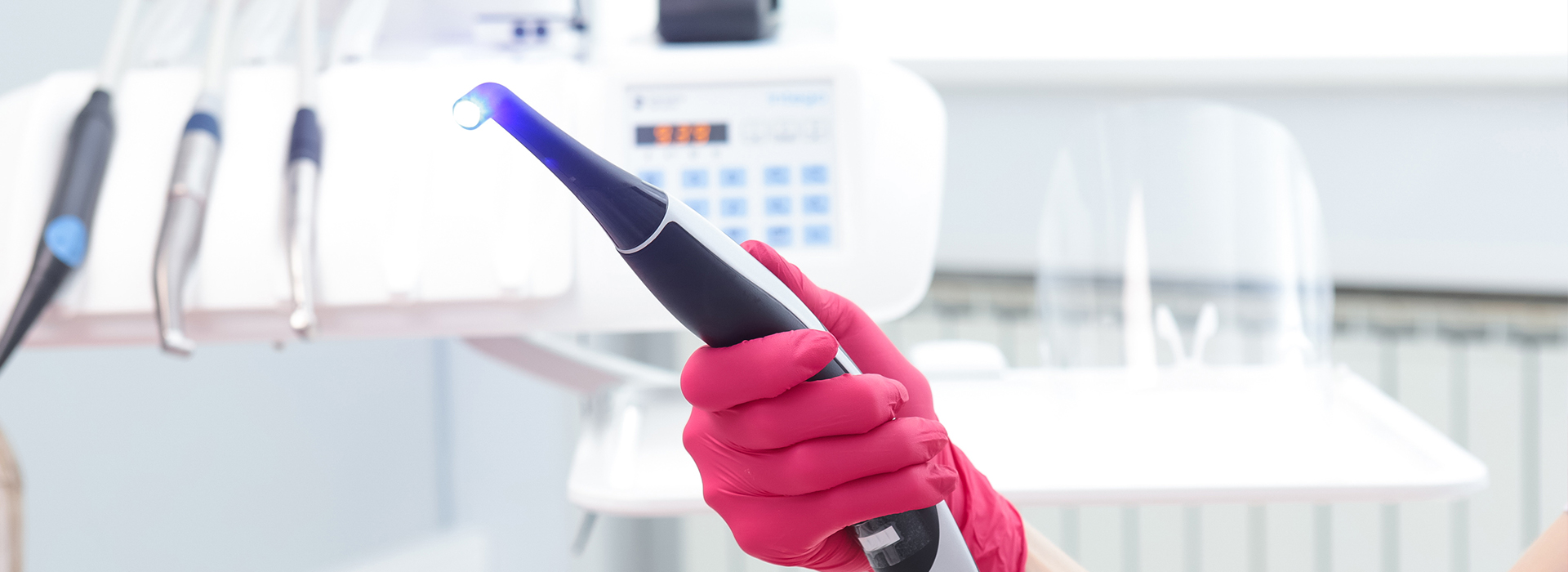 The image shows a person in a medical or dental setting, holding a blue device that appears to be a handheld ultrasonic cleaning tool. They are wearing pink gloves and are focused on the task at hand.