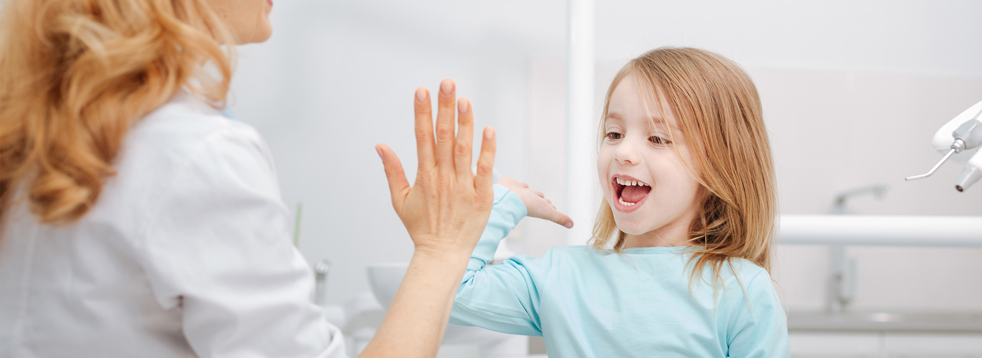 A young child with blonde hair is high-fiving a woman in a medical setting, both are smiling.